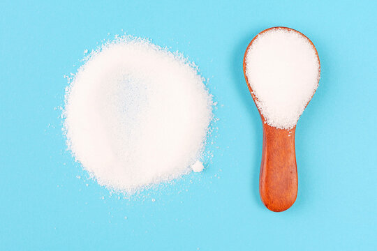 Erythritol powder in a wooden spoon close-up on blue background.