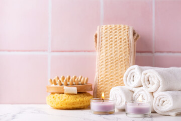 Fototapeta na wymiar Spa setting with burning canles, towels, wisk, massager against pink tiled wall. Beauty blogging, salon care concept. Selective focus. Place for text.