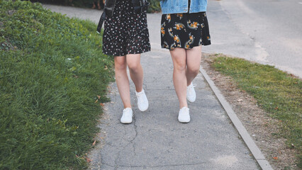 Two girlfriends in white sneakers walk down the street.