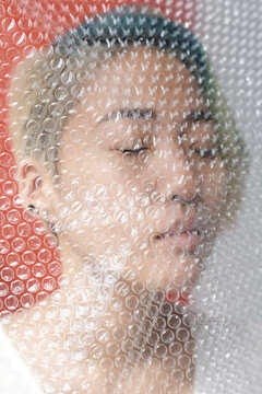 Close up portrait of Asian woman with her eyes closed standing behind bubble wrap