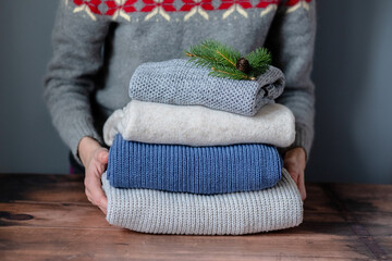 Female hands folding on a stack on a wooden table. Change of season and wardrobe. Winter slow fashion concept