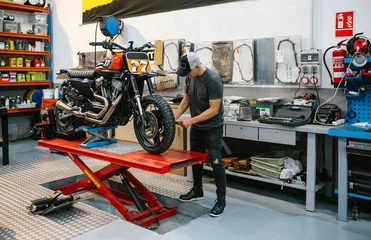 Fototapete Motorrad Unrecognizable mechanic man checking engine of custom motorcycle over platform on factory