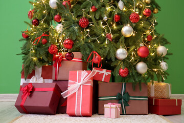 Fototapeta na wymiar Gifts under glowing Christmas tree near green wall