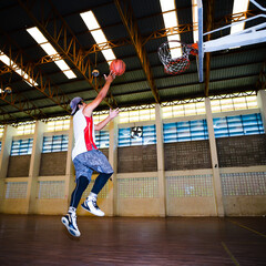 Asian basketball player jumping with basketball in hand.
