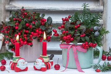 Fototapeta na wymiar Weihnachtsdekoration mit roten Kerzen, Weihnachtsmännern und Scheinbeeren in Emaille-Töpfen