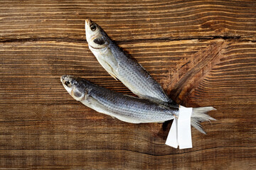 Two air-dried mullets with paper label on tails on wooden surface