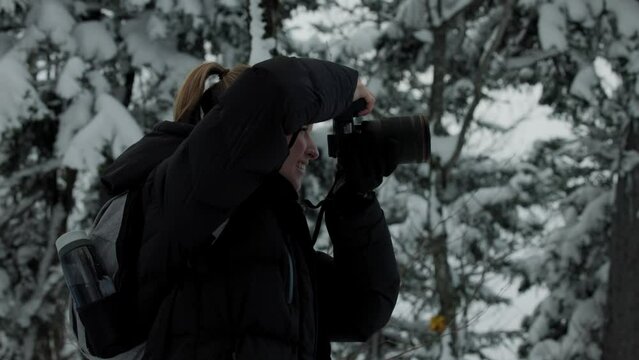Young Woman In Winter Clothes Holding A Digital Camera Taking Pictures In A Snowy Nature Landscape At Mont Chauve National Park, Orford, Quebec, Canada. - Medium Closeup