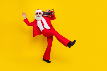 Fototapeta na wymiar Full length photo of excited funky santa dressed red suit tie walking enjoying boom box music empty space isolated yellow color background
