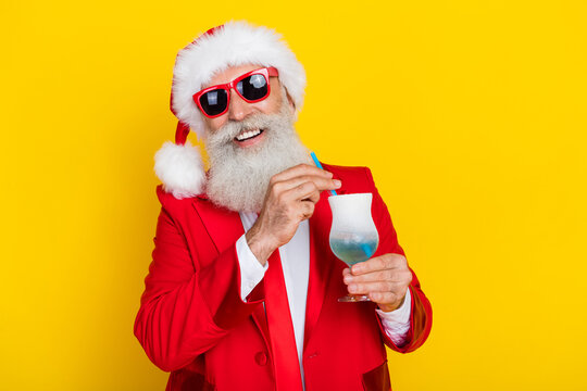 Photo of cheerful funny retired man dressed xmas suit dark eyewear drinking straw beverage isolated yellow color background