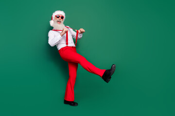Full length photo of cheerful positive senior guy wear red trousers dance nightclub go step empty space isolated on green color background