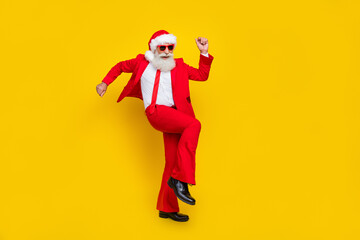 Fototapeta na wymiar Full length photo of positive lucky man pensioner dressed red suit santa hat having fun rising fist isolated yellow color background