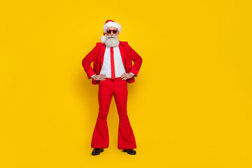 Fototapeta na wymiar Full length photo of serious confident retired guy wear red tux claus hat arms hands waist empty space isolated yellow color background