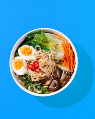 Ramen noodle soup with eggs, mushrooms, pak choi in hard light on orange