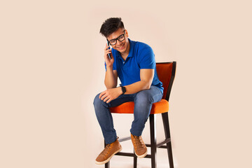 Young man talking on mobile phone while sitting on chair against white background