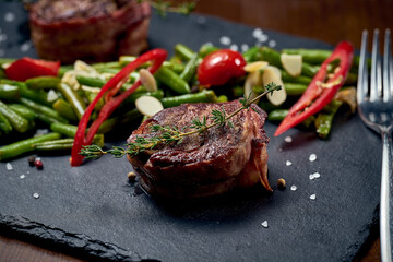 Filet mignon steak with vegetable garnish on a black board. Close-up, selective focus