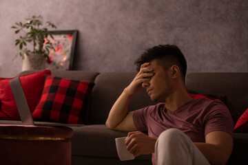 Portrait of a stressed young man leaning on sofa with hand on head in living room