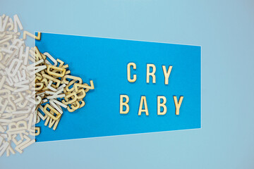 CRY BABY in wooden English language capital letters spilling from a pile of letters on a blue...