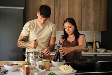 Fototapeta na wymiar Two young hispanic people preparing arepas in a pan at kitchen.