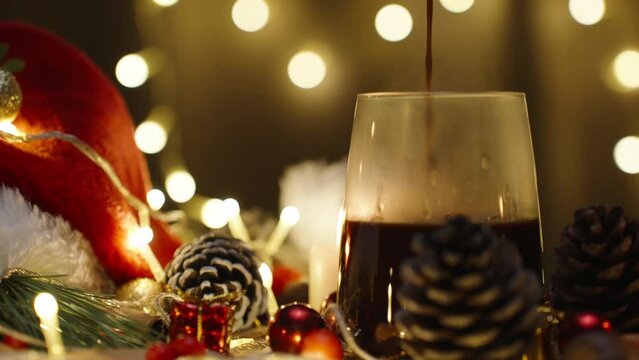 I pour hot chocolate, against the background of a garland of lights. Christmas table with candles and decorations. Slow motion.