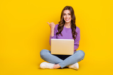 Naklejka premium Full length portrait of positive person sit floor use netbook direct thumb finger empty space isolated on yellow color background