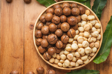 Macadamia nuts with leaf and Macadamia with hard shell on wooden plate on wooden background.