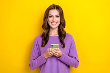 Photo of young satisfied pretty lady blogger hold her new apple iphone use for business convenient app montage isolated on yellow color background