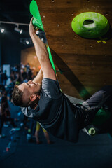 A young, athletic guy with a beautiful inflated body climbs a bouldering in a climbing hall. Emotions on the face.