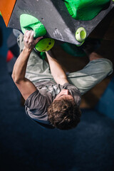 A young, athletic guy with a beautiful inflated body climbs a bouldering in a climbing hall. Emotions on the face.