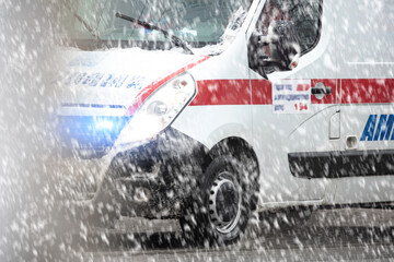 911 ambulance van rushing through traffic during heavy winter snowfall conditions. © astrosystem