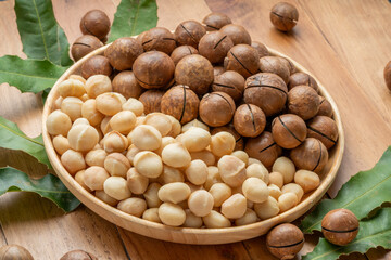 Macadamia nuts with leaf and Macadamia with hard shell on wooden plate on wooden background.