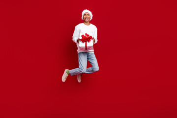 Full length photo of excited cheerful person jumping hands hold newyear giftbox isolated on red color background