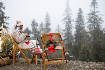 Young woman relaxes and enjoys calm on nature during winter holidays, has a picnic while traveling by car in mountains. Concept of celebrating New Year alone on nature