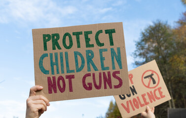 Protesters holding signs with slogans Protect Children Not Guns and Stop Gun Violence. People with...
