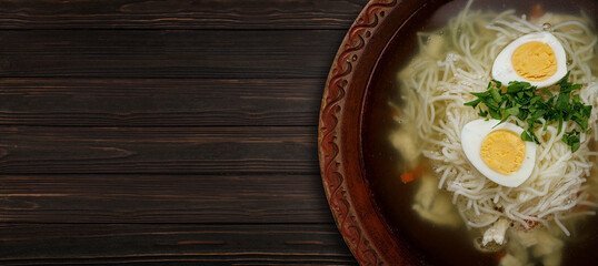 Chicken broth, with noodles, herbs and egg, on a wooden background