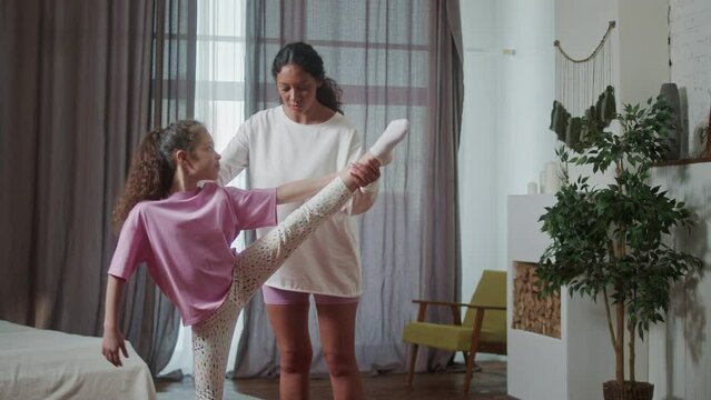 Young Hispanic Woman teach doing stretching exercises training her little cute daughter in cozy living room perform. Happy activity in family concept.