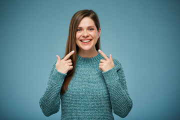Smiling woman pointing at her teeth. Advertising female studio portrait on blue. - 552019823
