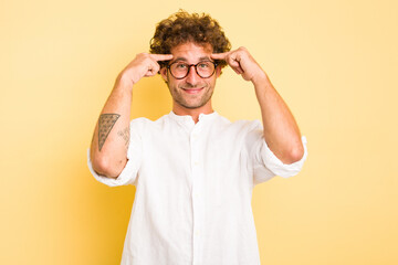 Young smart caucasian man on yellow background focused on a task, keeping forefingers pointing head.