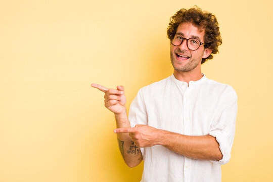 Young smart caucasian man on yellow background excited pointing with forefingers away.