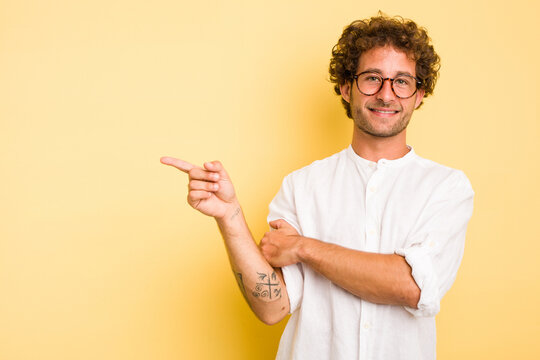 Young smart caucasian man on yellow background smiling cheerfully pointing with forefinger away.