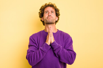 Young smart caucasian man on yellow background holding hands in pray near mouth, feels confident.