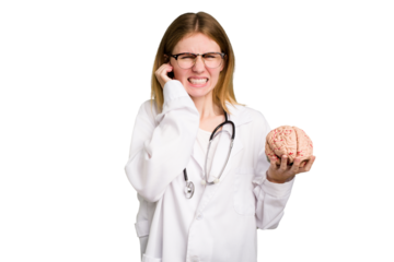 Young doctor caucasian woman holding a brain isolated covering ears with hands.
