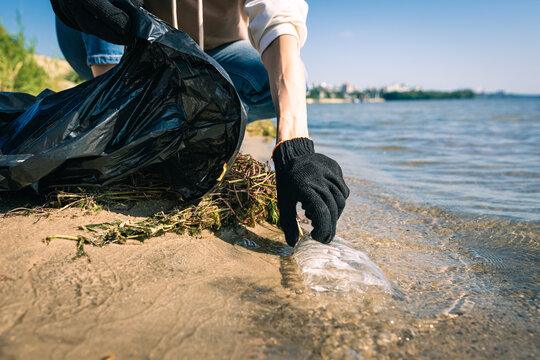 Woman picking up garbage on the beach. Cleaner collecting garbage on the sand beach into black plastic bag