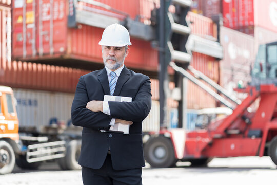 Portrait of senior foreman or supervisor container yard worker working and standing with crane forklift truck blur background at commercial dock site