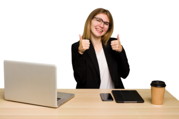 Young business caucasian woman working on her workplace cutout isolated raising both thumbs up, smiling and confident.