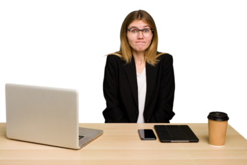 Young business caucasian woman working on her workplace cutout isolated shrugs shoulders and open eyes confused.