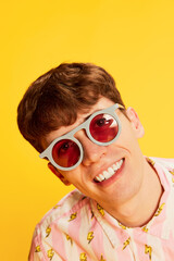 Closeup portrait of astonished young man in fashionable eyewear smiling isolated over bright yellow background. Youth culture, positive emotions