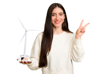 Young caucasian woman holding a small wind energy mill isolated joyful and carefree showing a peace symbol with fingers.