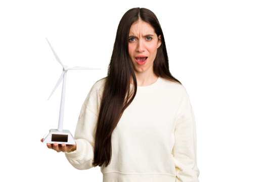 Young caucasian woman holding a small wind energy mill isolated screaming very angry and aggressive.