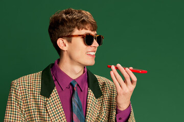 Studio footage young man in vintage fashion style costume talking on smartphone isolated on dark...