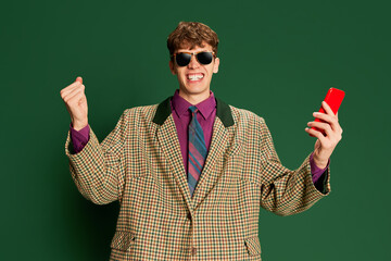 Studio footage young man in vintage fashion style costume, suit posing isolated on dark green background. Concept of retro style, creativity, emotions, facial expression, fashion